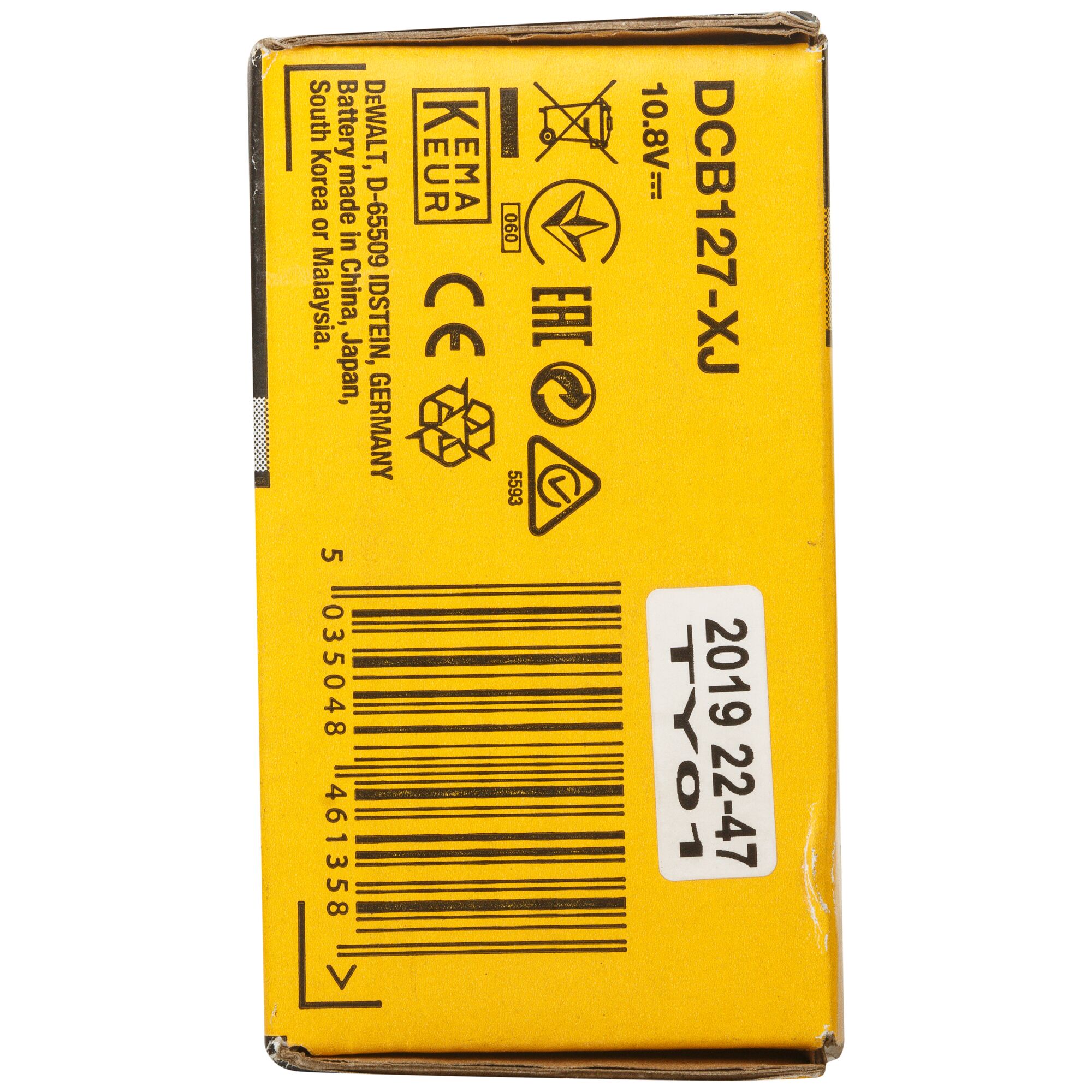 Close-up of a yellow DEWALT product box showing various certification symbols, barcode, and product code DCB127-XJ. The box displays information indicating the battery is made in China, Japan, South Korea, or Malaysia. The text also specifies 10.8V and includes a sticker with '2019 22-47 TY01'.