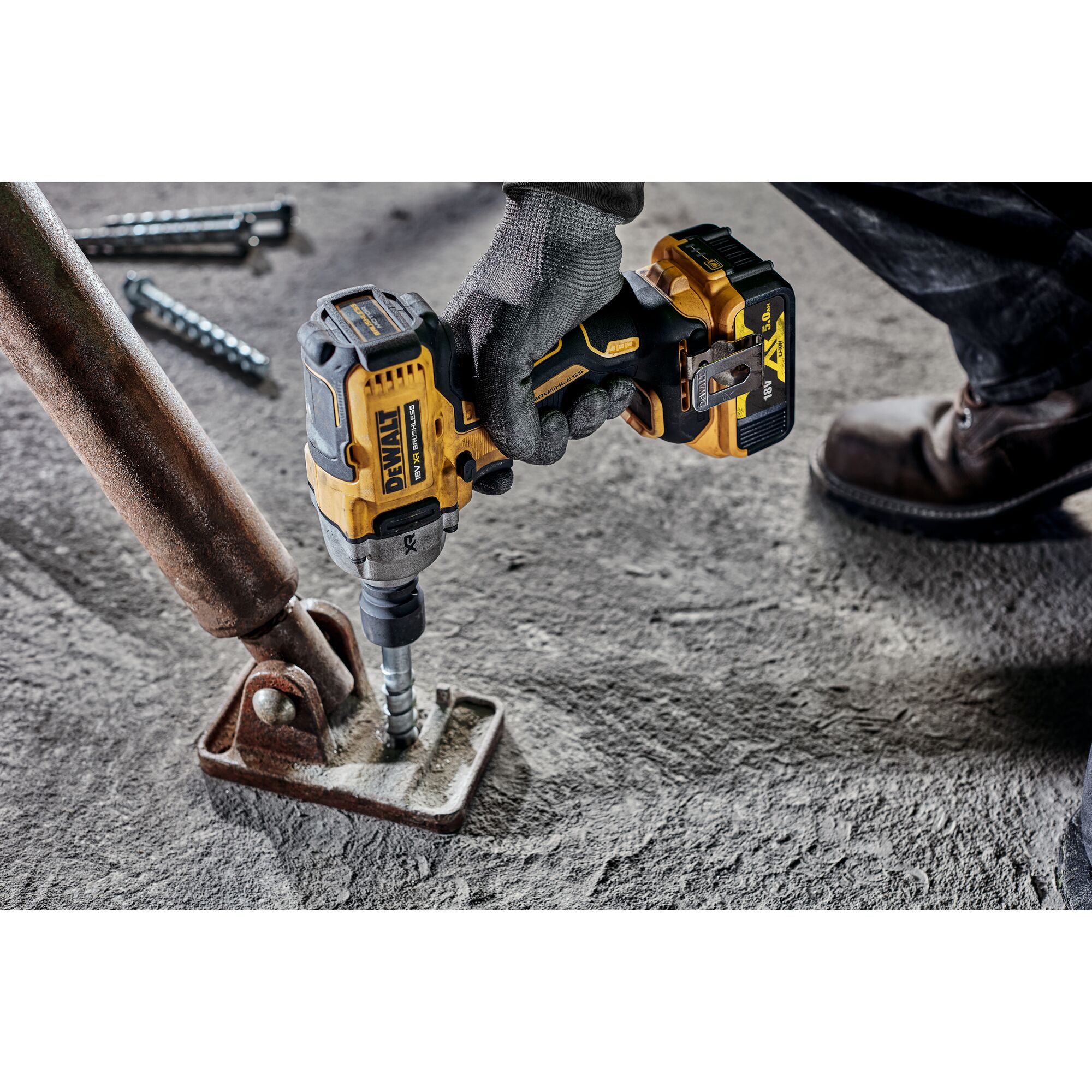 A DEWALT cordless impact wrench being used by a person wearing gloves, fastening a bolt to a metal base on a concrete surface.