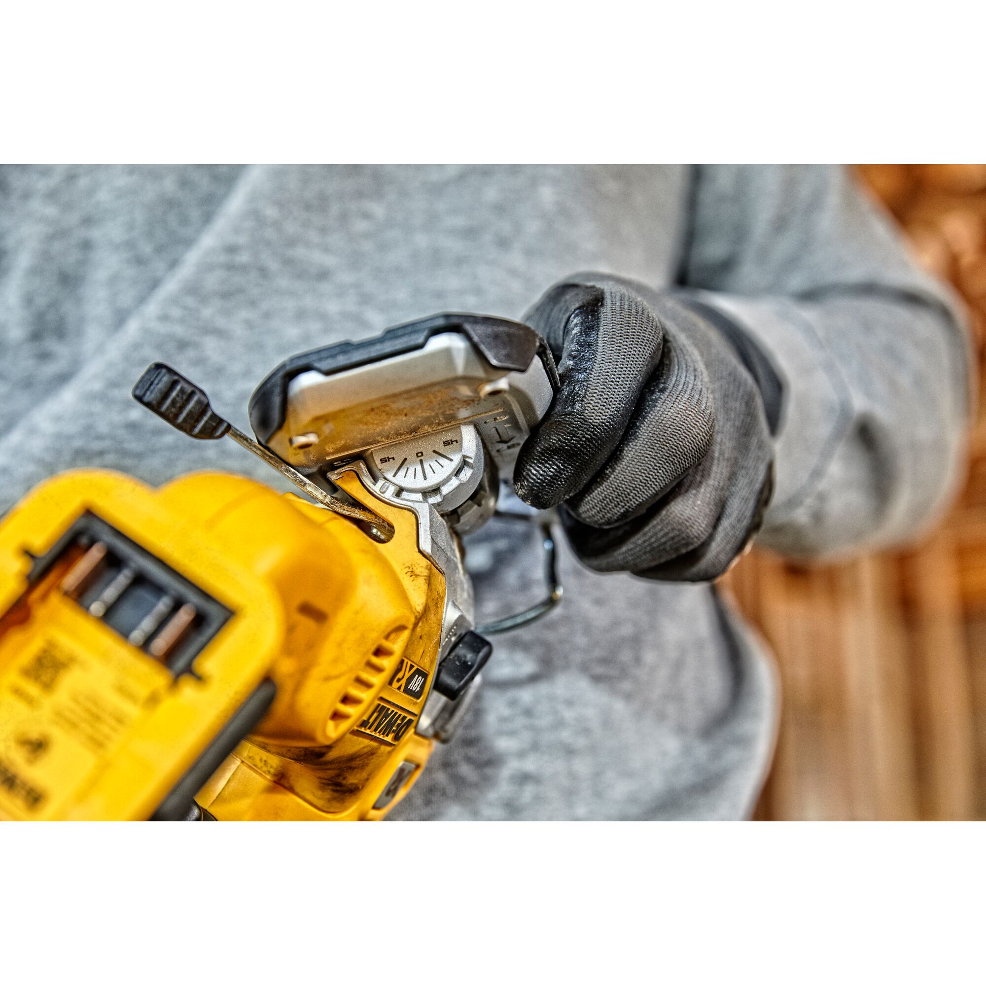 Close-up of a person wearing black gloves adjusting the angle on a yellow DEWALT power tool, specifically a cordless jigsaw.