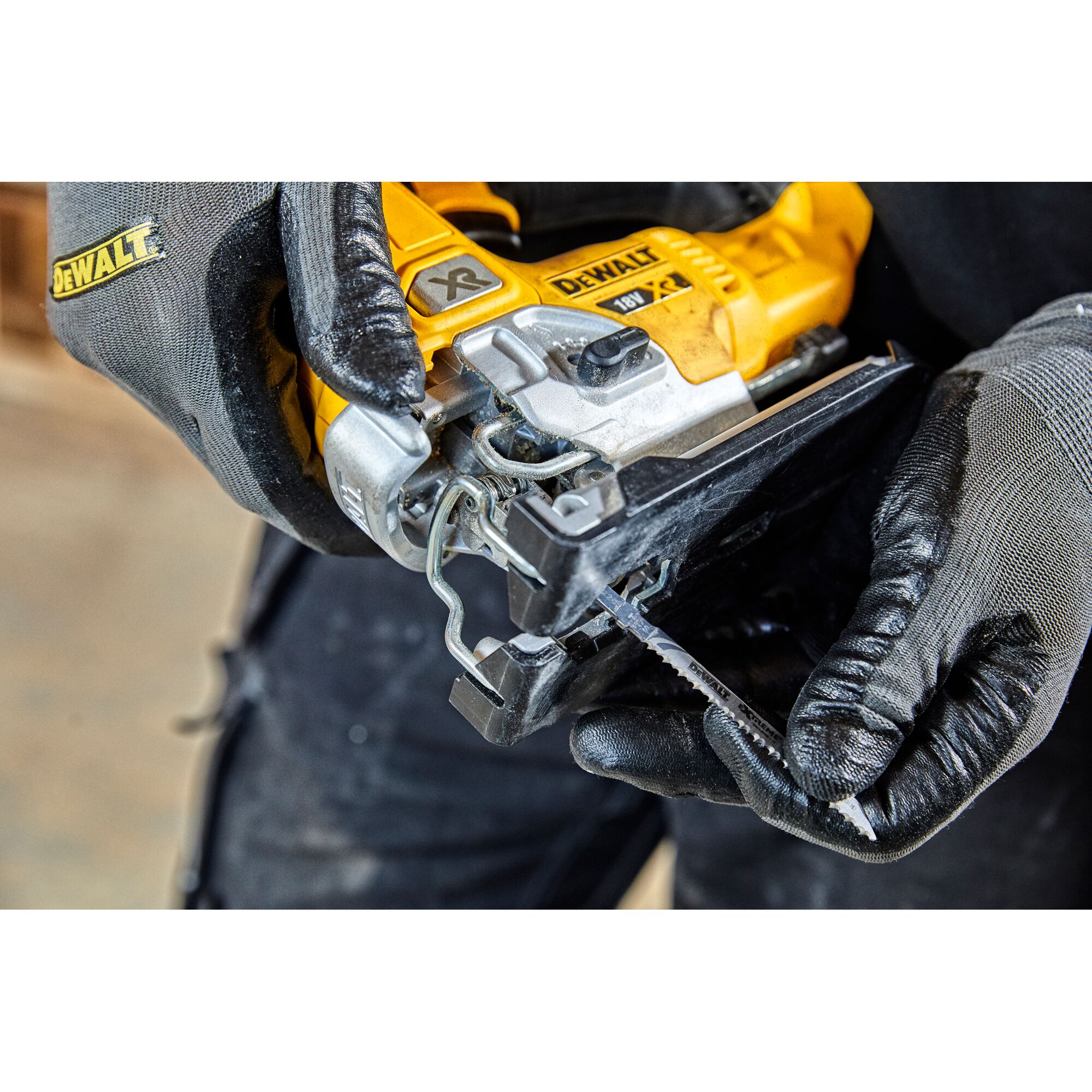 Close-up of a person wearing gloves inserting a saw blade into a DEWALT cordless jigsaw tool.